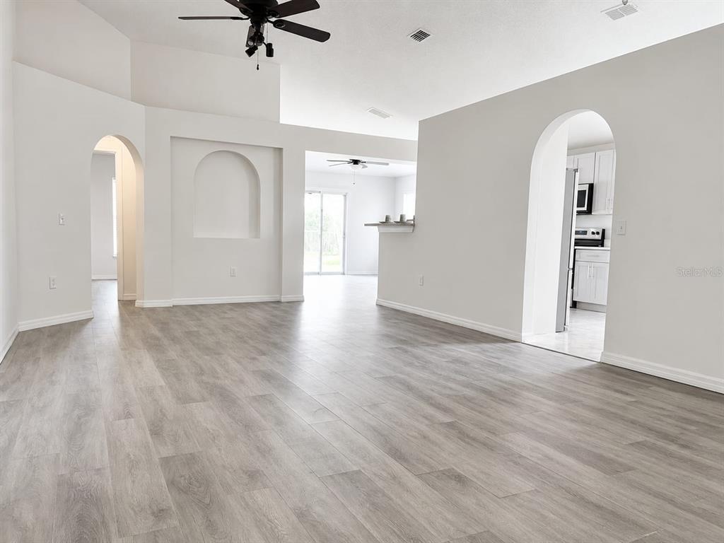 A living room with light wood-look flooring, white walls, and arched doorways leading to other rooms — 210 FAIRFIELD DRIVE, SANFORD, FL