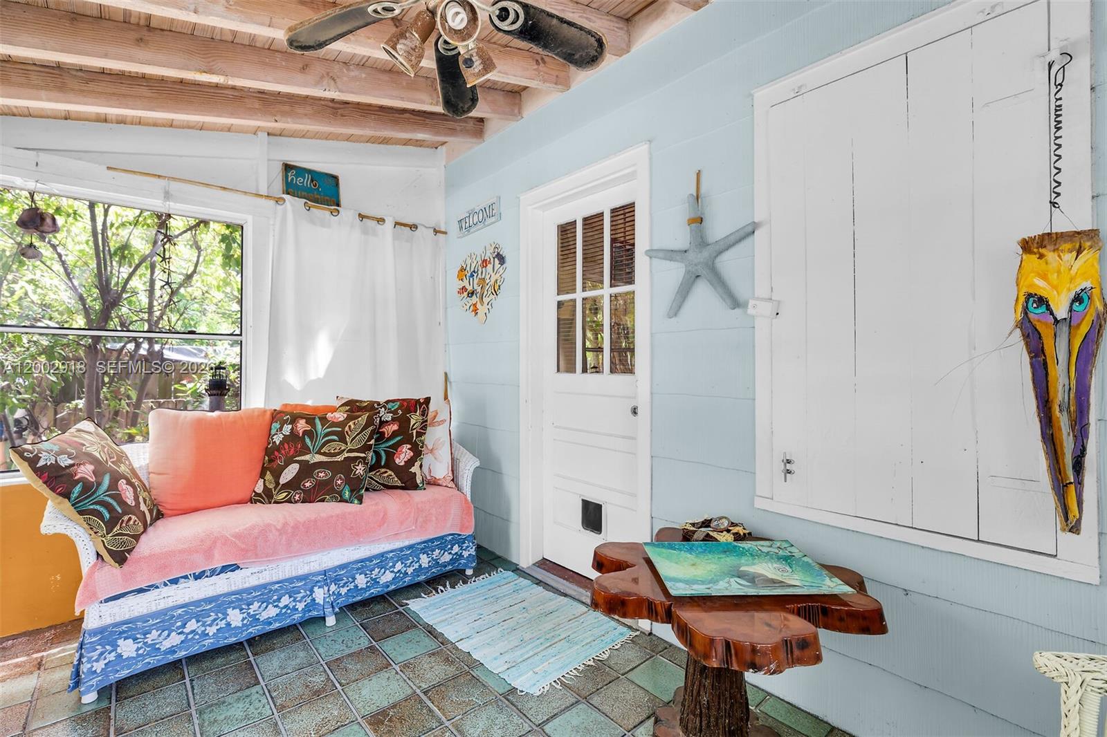 A sunroom features a daybed, a wooden pedestal table, and a light blue wall — 140 Tavern Dr, Tavernier FL 33070, TAVERNIER, FL
