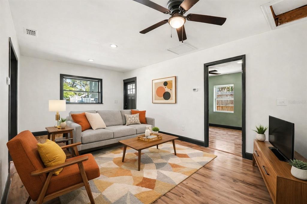 A living room features a grey sofa, orange armchair, wood flooring, and a ceiling fan — 1221 E EMMA STREET, TAMPA, FL