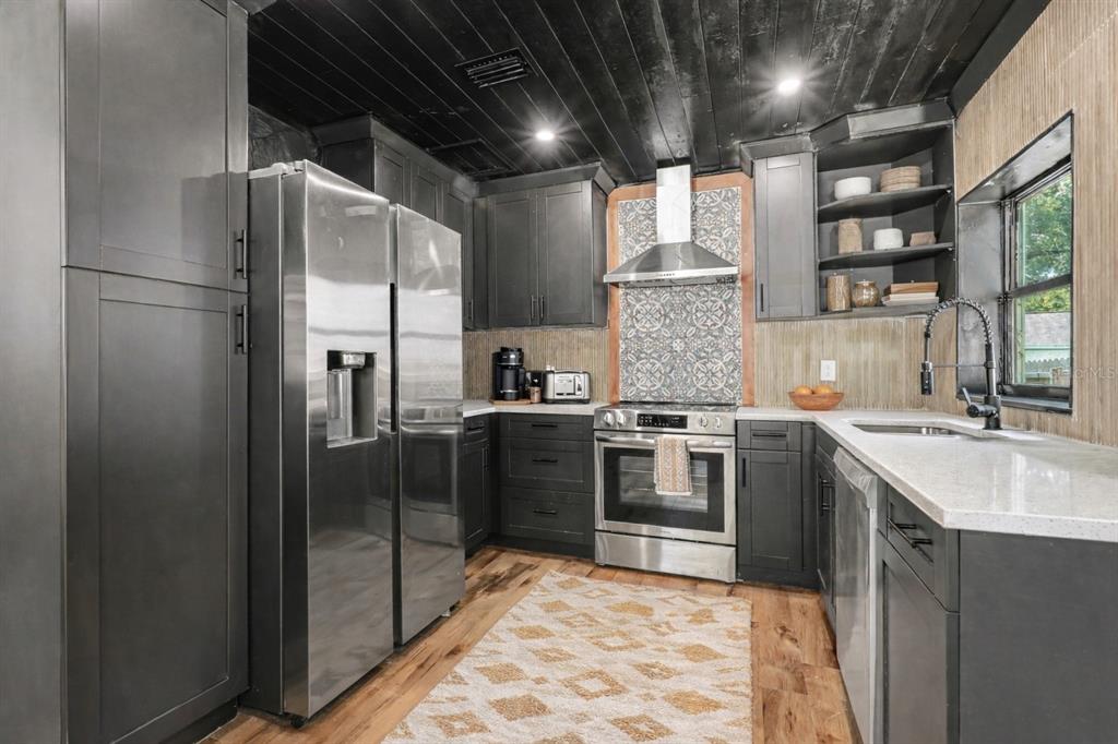 A kitchen features dark cabinets, stainless steel appliances, a patterned backsplash, and a wood ceiling — 1221 E EMMA STREET, TAMPA, FL
