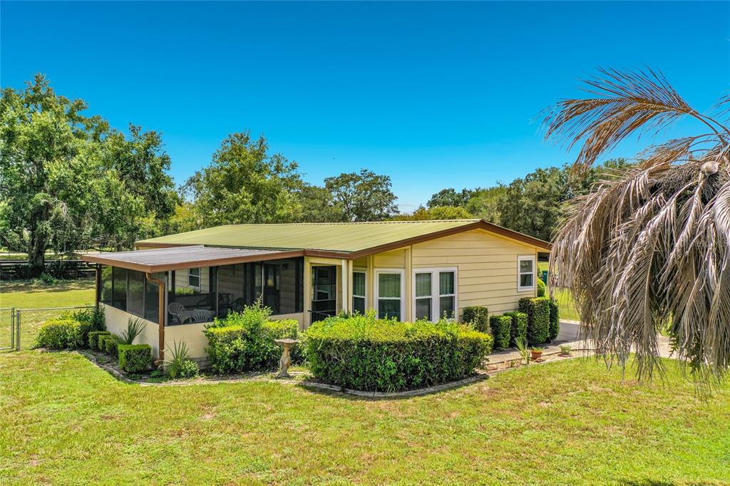 A single-story house with yellow siding and a screened-in porch sits on a grassy lot — 8233 COUNTY ROAD 109B, LADY LAKE, FL