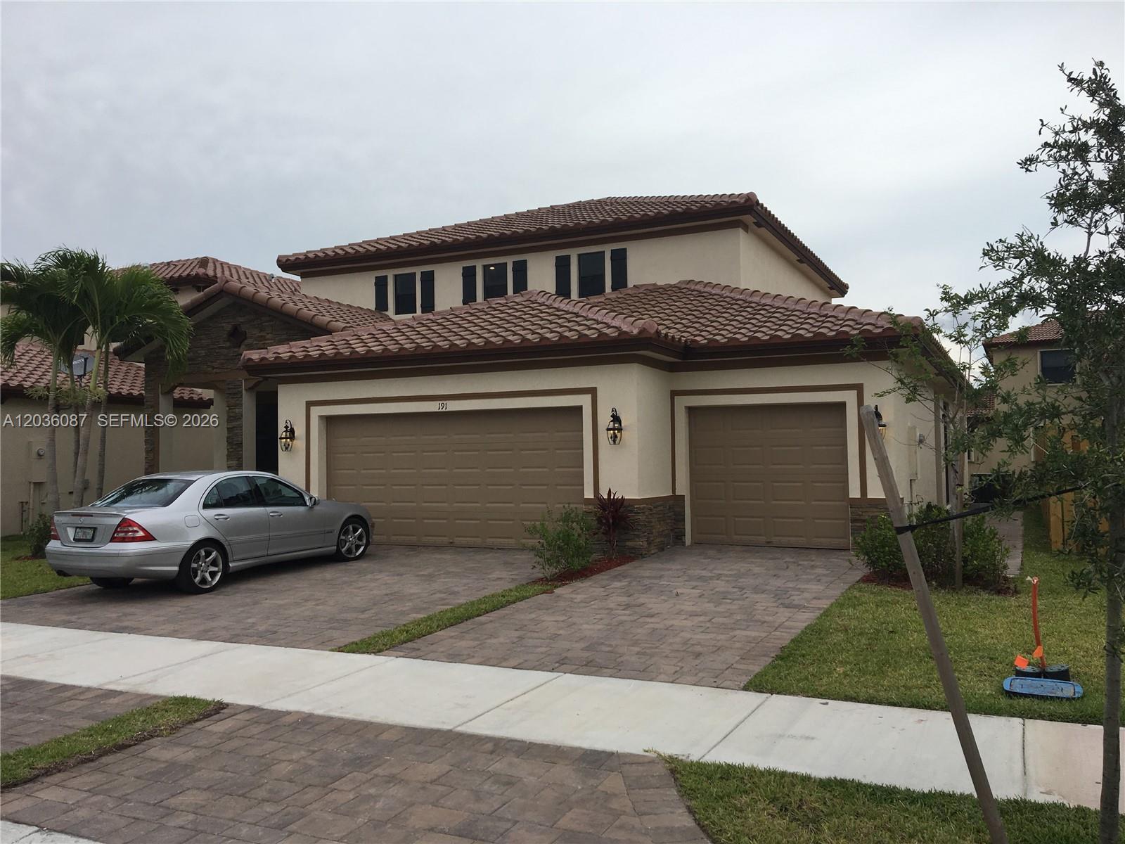 A two-story house with a three-car garage and a paved driveway under a cloudy sky — 191 SE 35th Ave, Homestead FL 33033, HOMESTEAD, FL