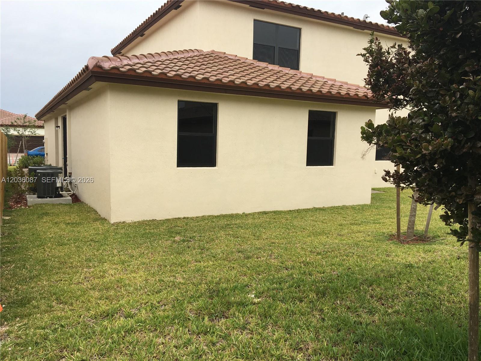 The exterior of a two-story beige stucco house features a tiled roof and two windows — 191 SE 35th Ave, Homestead FL 33033, HOMESTEAD, FL