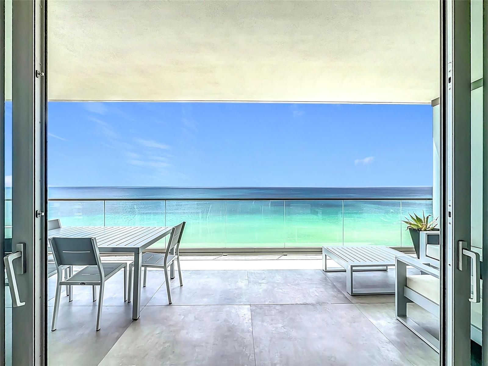 A balcony with outdoor furniture overlooks the ocean through a glass railing — 2000 S Ocean Drive # 12A, Hallandale Beach FL 33009, HALLANDALE BEACH, FL