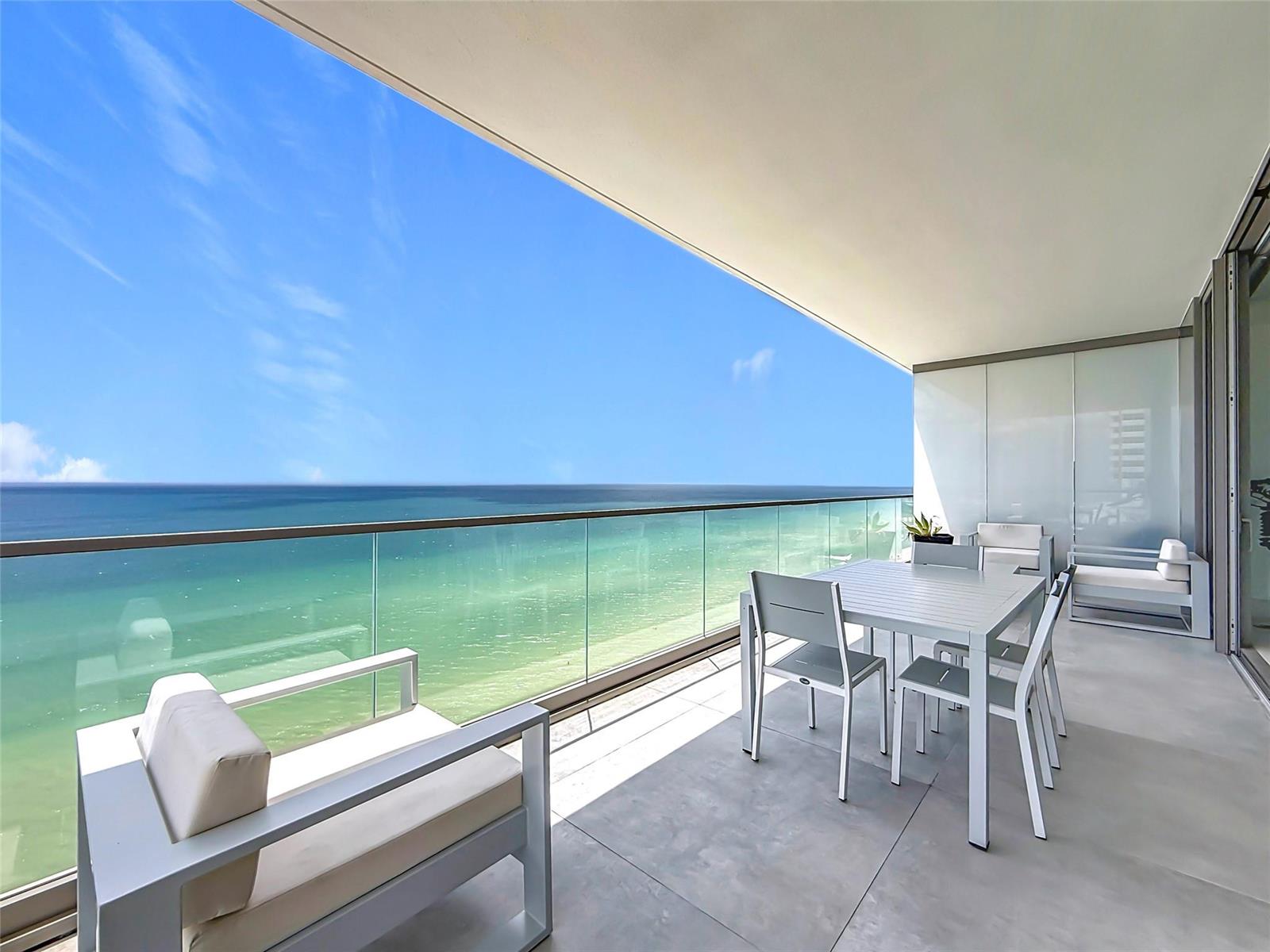 A modern balcony features a dining set, lounge chairs, and a glass railing overlooking the ocean — 2000 S Ocean Drive # 12A, Hallandale Beach FL 33009, HALLANDALE BEACH, FL