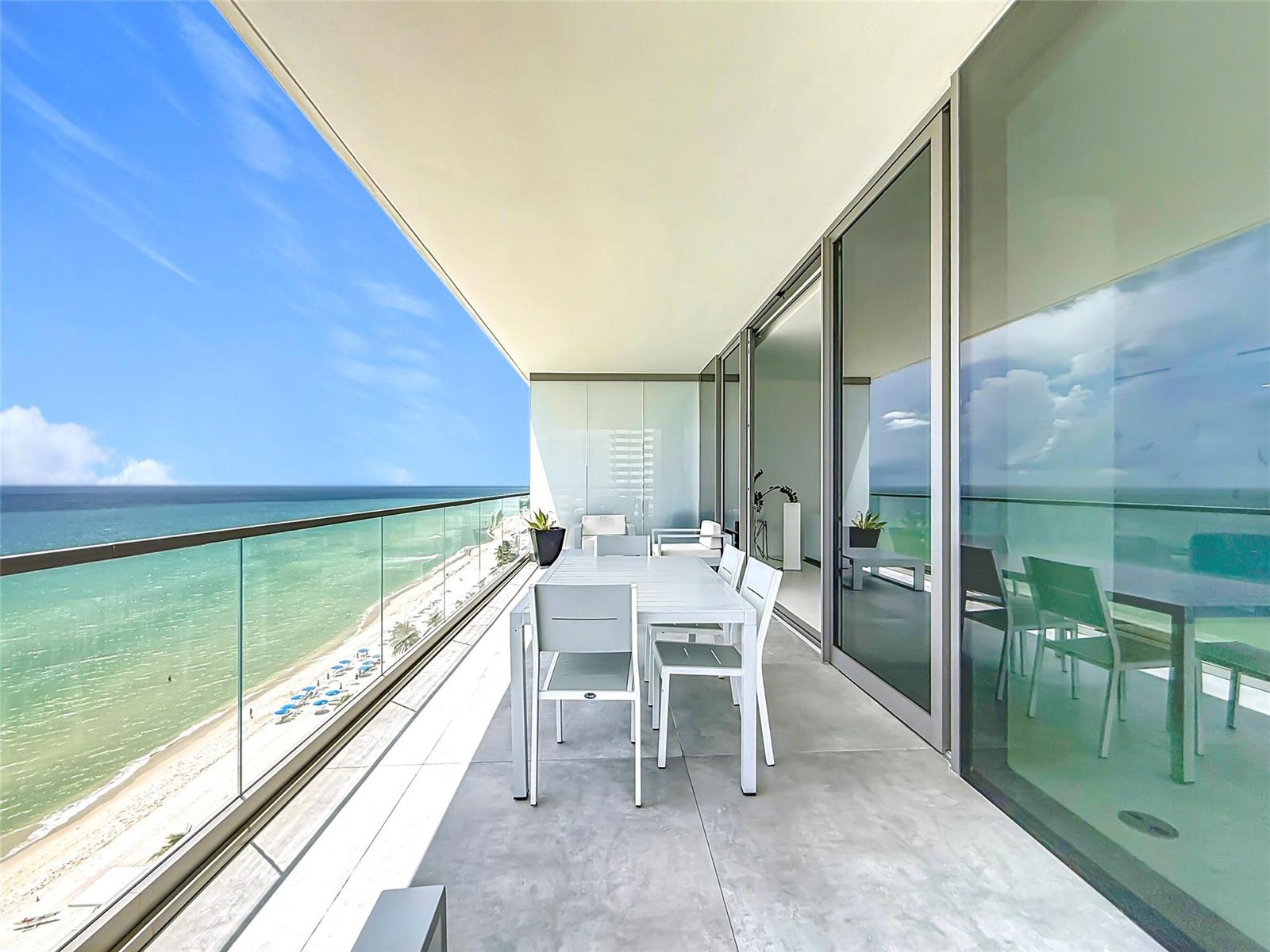 A modern balcony features a dining set, glass railings, and a panoramic ocean view — 2000 S Ocean Drive # 12A, Hallandale Beach FL 33009, HALLANDALE BEACH, FL