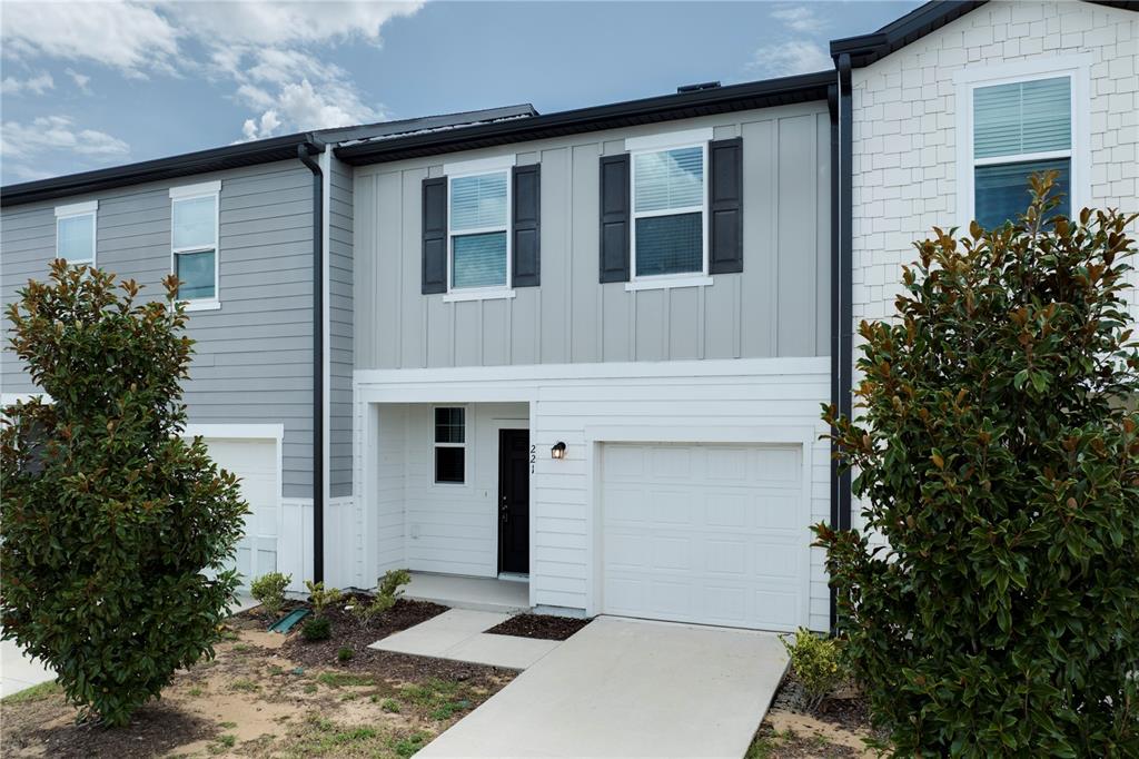 A two-story townhouse exterior features a white garage, a black front door, and gray siding — 221 MANDOVI STREET, DAVENPORT, FL