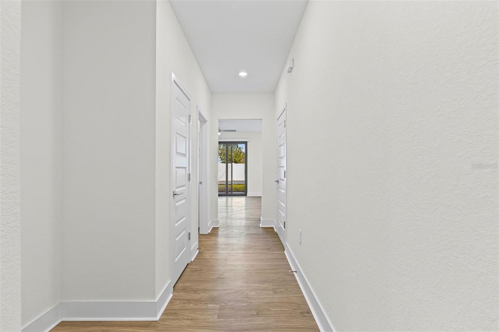 A hallway with light wood-look flooring leads to a doorway with a view of outdoors — 14515 STELLAR PLACE, LAKEWOOD RANCH, FL
