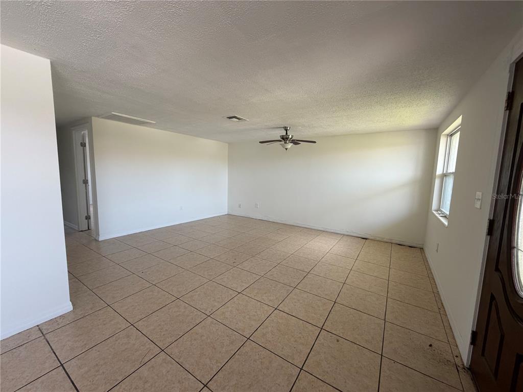 An empty living room features beige tile flooring, white walls, and a ceiling fan — 4138 STAR ISLAND DRIVE, HOLIDAY, FL