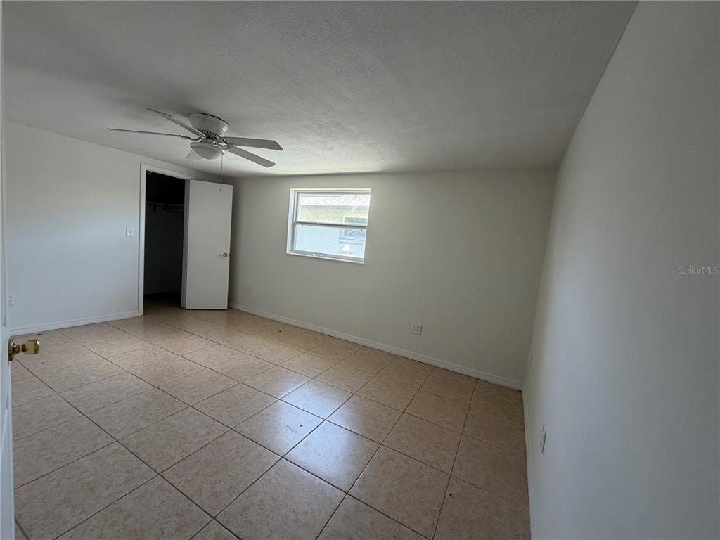 An empty bedroom features light-colored tile flooring, white walls, a ceiling fan, and a closet — 4138 STAR ISLAND DRIVE, HOLIDAY, FL