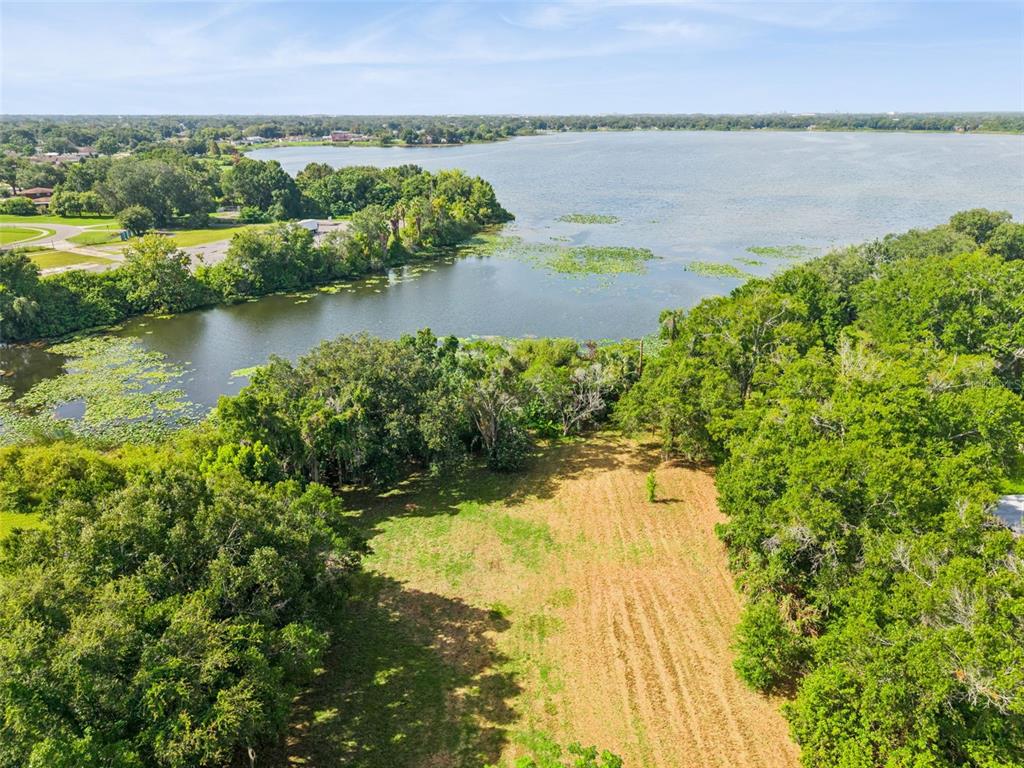 An aerial view shows a cleared grassy lot bordered by dense trees and a lake — 3524 W ROBINSON STREET, ORLANDO, FL