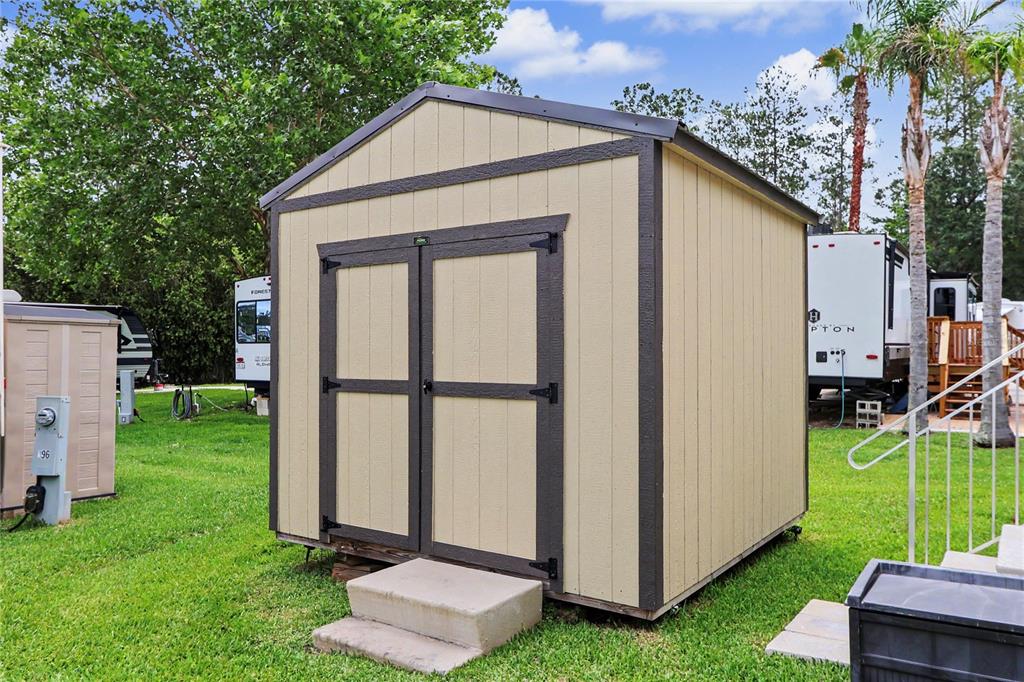 A beige wooden storage shed with dark brown trim sits on a grassy lawn — 2923 NE 104TH AVENUE, SILVER SPRINGS, FL