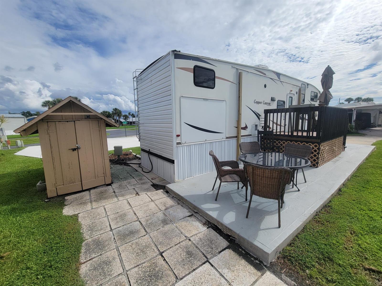 A Copper Canyon travel trailer sits on a concrete patio next to a wooden shed — 6571 SE 55th Lane, Okeechobee FL 34974, OKEECHOBEE, FL