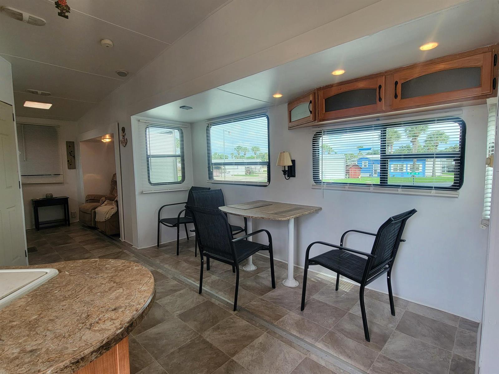 A dining area in a mobile home features a table, three chairs, and overhead cabinets — 6571 SE 55th Lane, Okeechobee FL 34974, OKEECHOBEE, FL