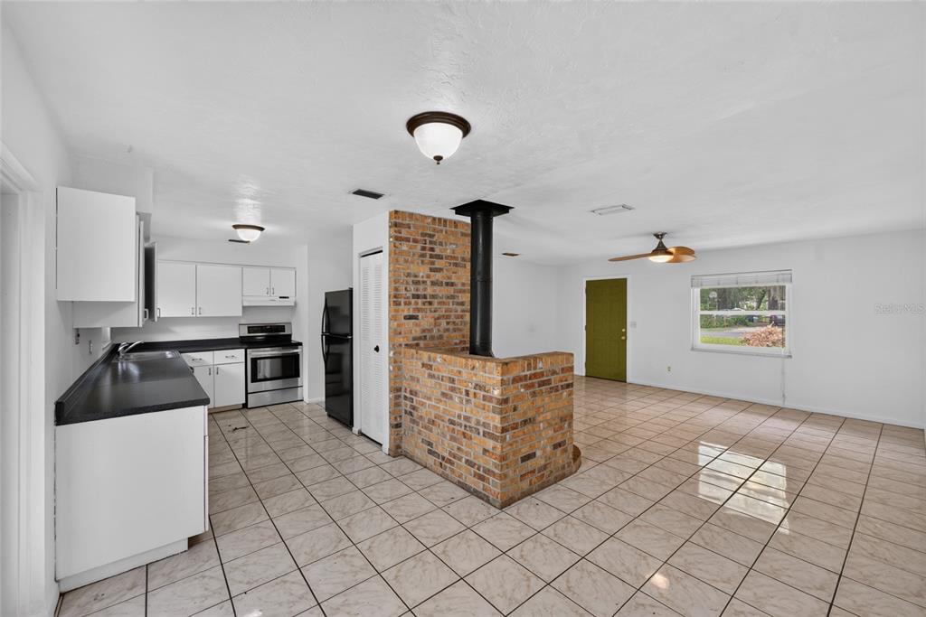 A kitchen and living area with tile floors, white cabinets, and a central brick fireplace — 4820 NE 4TH PLACE, GAINESVILLE, FL
