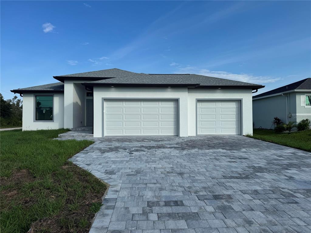 A modern single-story house with a white stucco exterior and a gray paver driveway — 9309 ZORN STREET, PORT CHARLOTTE, FL