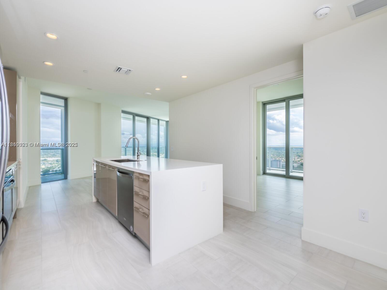 A modern kitchen features a white island with a sink, stainless appliances, and light flooring — 2000 Metropica Way # 2509, Sunrise FL 33323, SUNRISE, FL