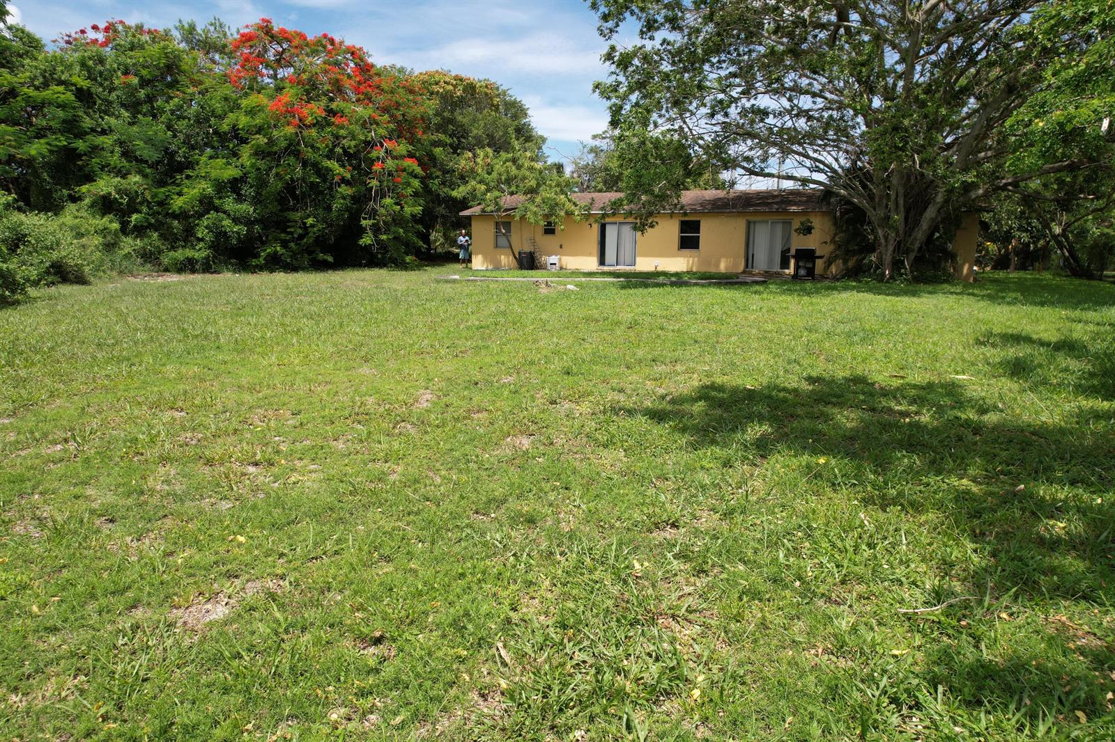 A yellow single-story house sits behind a large, grassy backyard with mature trees — 4537 Coconut Road, Lake Worth FL 33461, LAKE WORTH, FL