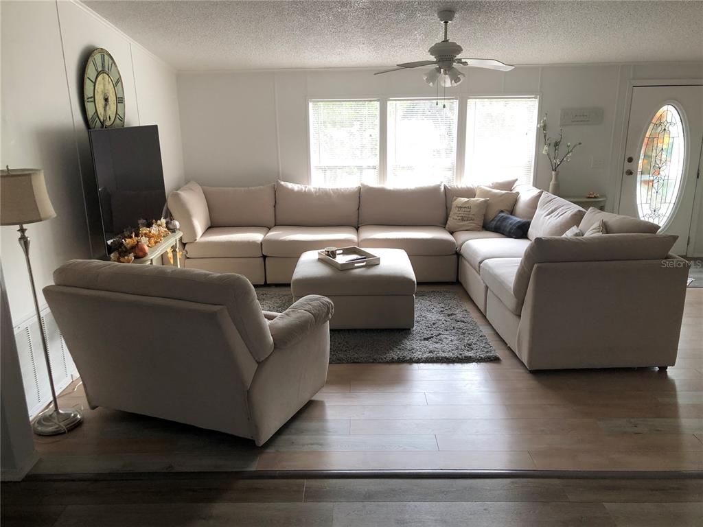 A living room features a large beige sectional sofa, matching armchair, ottoman, and light wood flooring — 265 W MCCLENDON ST, LADY LAKE, FL