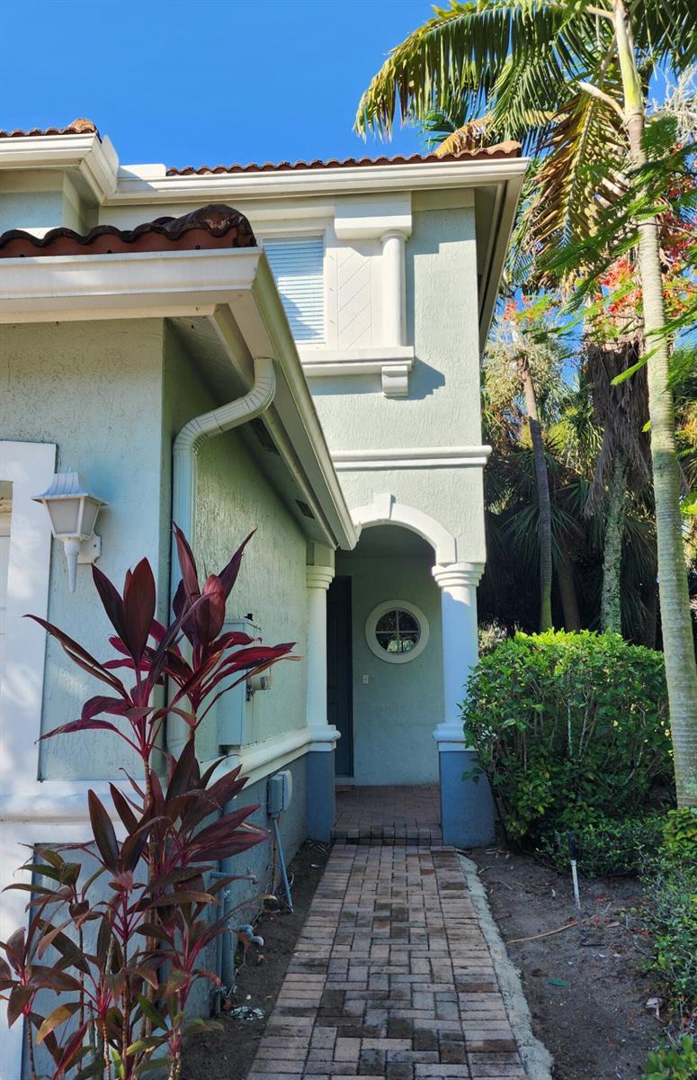 A paved walkway leads to the covered entrance of a two-story light green stucco home — 2124 Oakmont Drive, Riviera Beach FL 33404, RIVIERA BEACH, FL