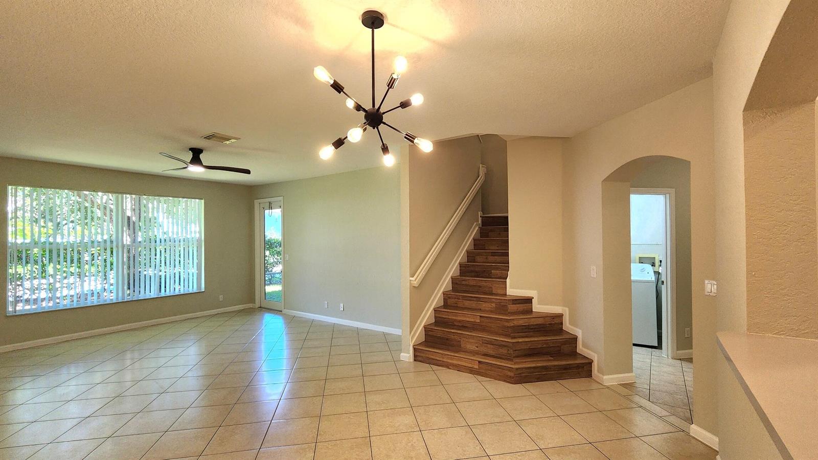 A living area with tile floors, a modern chandelier, and a wood-tread staircase — 2124 Oakmont Drive, Riviera Beach FL 33404, RIVIERA BEACH, FL