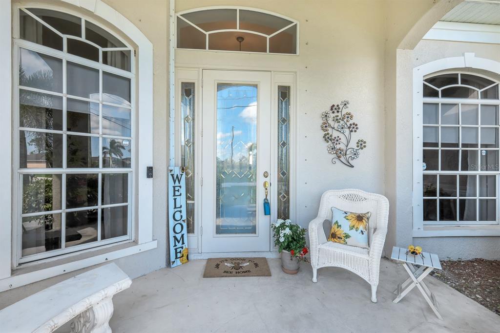A covered front porch features a white door, two large arched windows, and wicker furniture — 1206 NW 18TH TERRACE, CAPE CORAL, FL