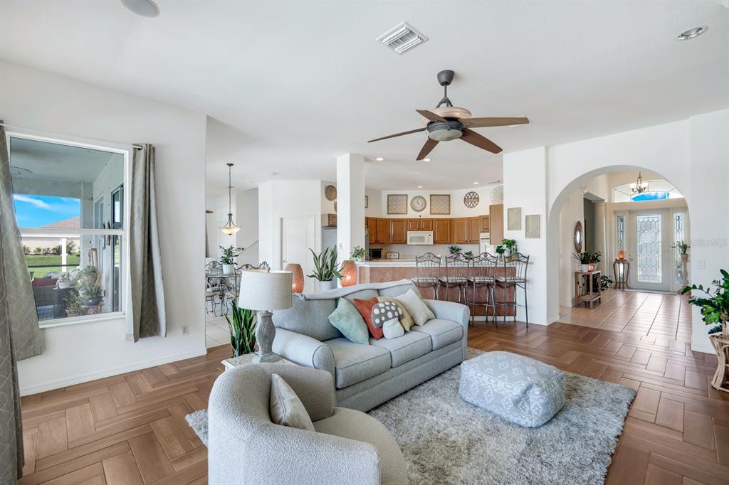 A living room with wood-look tile flooring, a gray sofa, and an open-concept kitchen — 1206 NW 18TH TERRACE, CAPE CORAL, FL