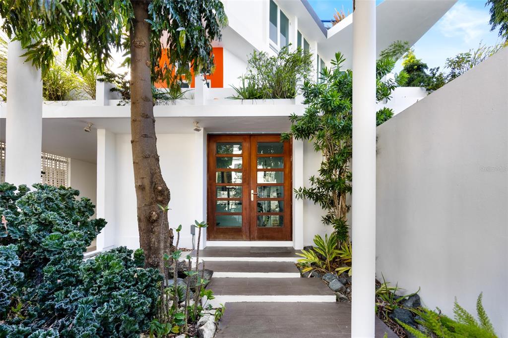 A modern house entrance features a wooden double door, white walls, and lush landscaping — 424 DEL VALLE ST MONTEFLORES DEV, SAN JUAN, PR