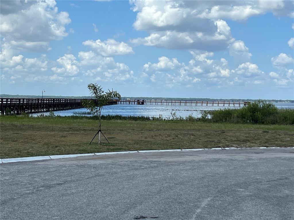 A long wooden pier extends into a lake under a blue sky with clouds — 506 MAGNOLIA DRIVE, INDIAN LAKE ESTATES, FL