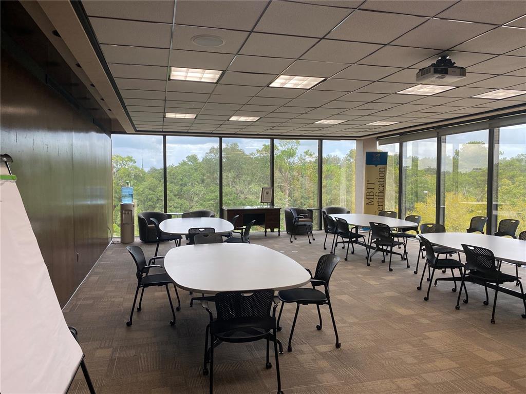 A conference room features multiple tables, black chairs, large windows, and a drop ceiling — 2815 NW 13TH STREET 4th Floor, GAINESVILLE, FL