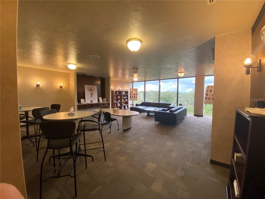 A common area features tables, chairs, a sofa, bookshelves, and large windows with outdoor views — 2815 NW 13TH STREET 4th Floor, GAINESVILLE, FL