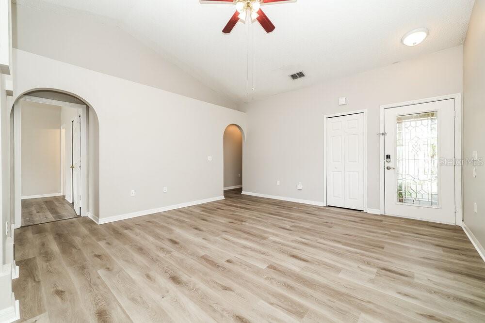 An empty living room features light-colored walls, wood-look flooring, arched doorways, and a ceiling fan — 6215 CANNOLI PLACE, RIVERVIEW, FL