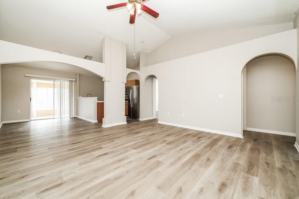 A spacious living room features vaulted ceilings, light wood-look flooring, and arched doorways — 6215 CANNOLI PLACE, RIVERVIEW, FL