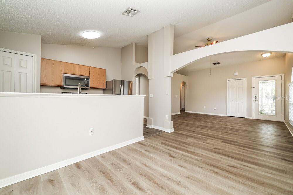 A kitchen with wood cabinets overlooks a living area with light wood-look flooring — 6215 CANNOLI PLACE, RIVERVIEW, FL