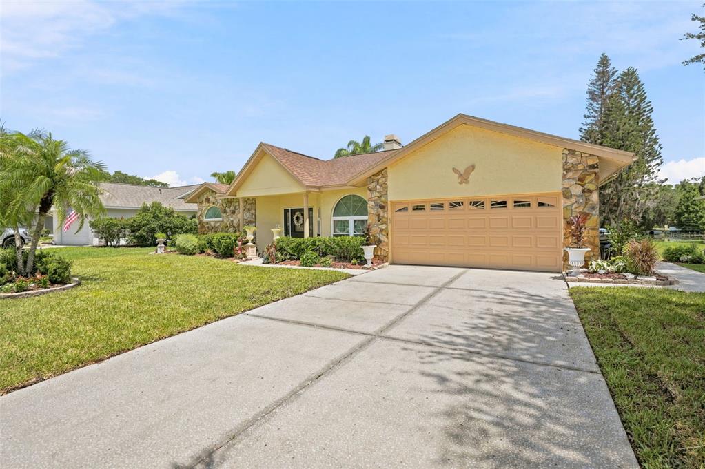 A single-story yellow house with a stone-accented garage and a concrete driveway — 23427 PINE LAKE STREET, LAND O LAKES, FL