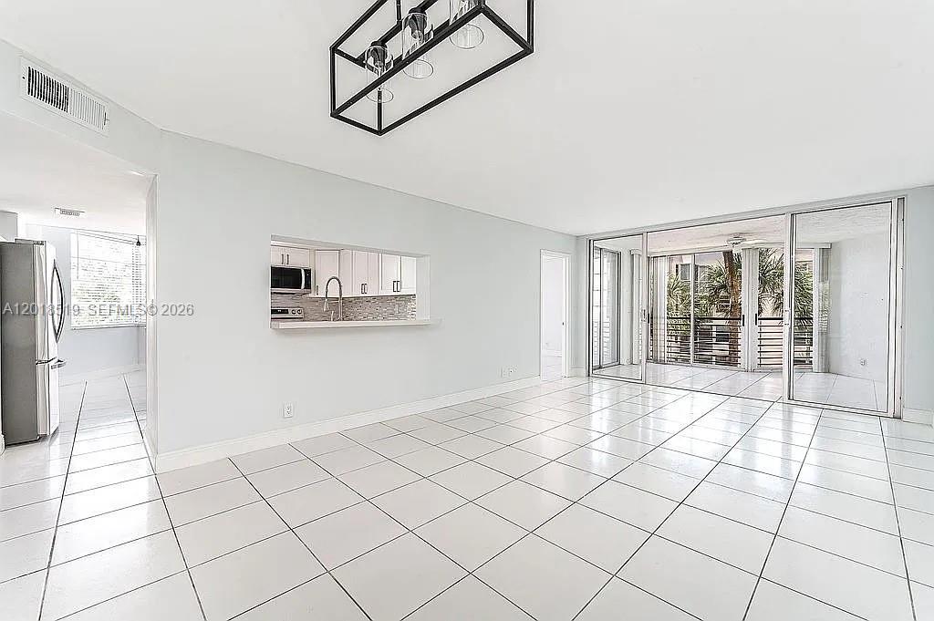 A bright, tiled living area features a kitchen pass-through window and sliding glass balcony doors — 1931 Sabal Palm Dr # 301, Davie FL 33324, DAVIE, FL