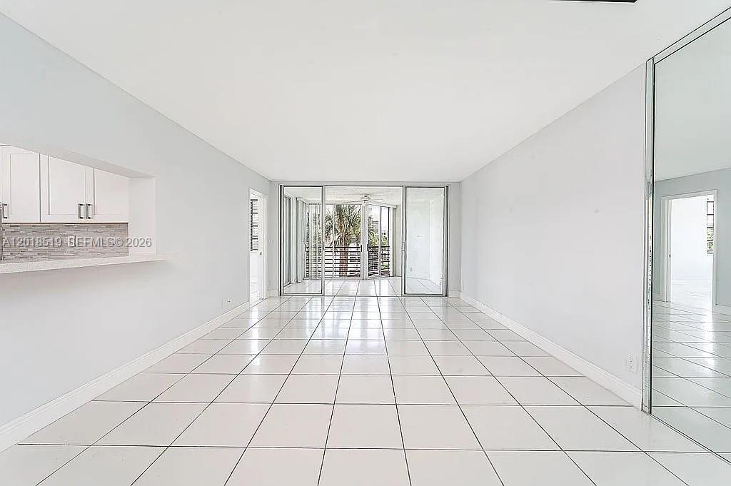 A bright, empty living room features white tile flooring, a kitchen pass-through, and sliding doors — 1931 Sabal Palm Dr # 301, Davie FL 33324, DAVIE, FL