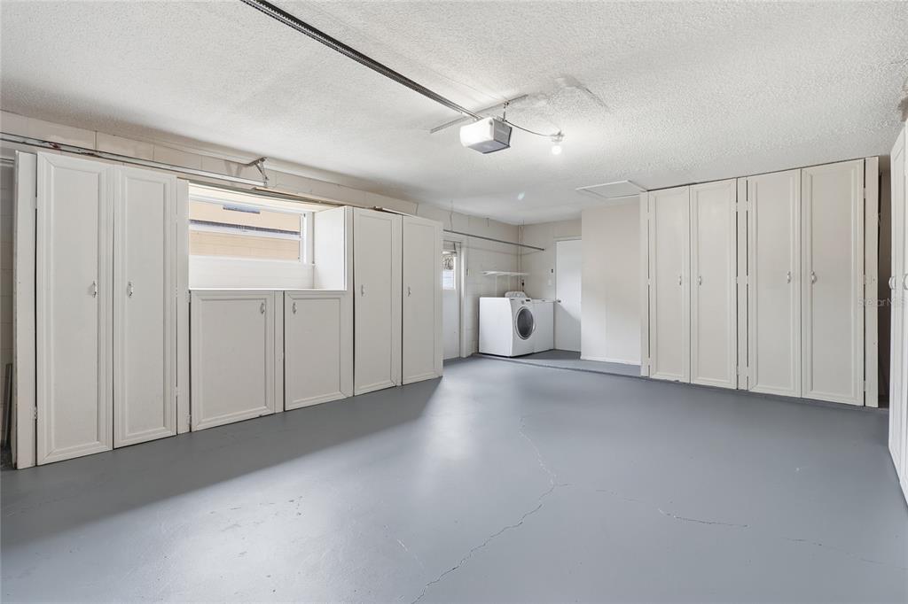 A garage with gray painted concrete floors, white storage cabinets, and a laundry area — 804 CENTERWOOD COURT, BRANDON, FL