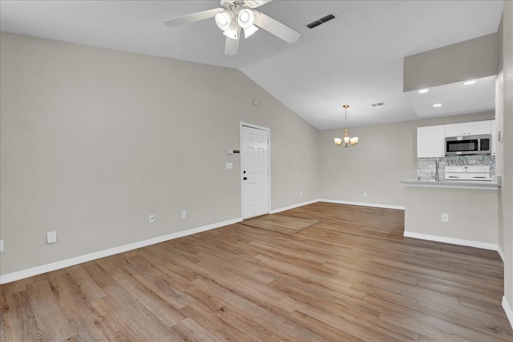 An open-concept living area features vaulted ceilings, wood-look flooring, and an adjacent kitchen — 8915 LATREC AVENUE UNIT 2311, ORLANDO, FL