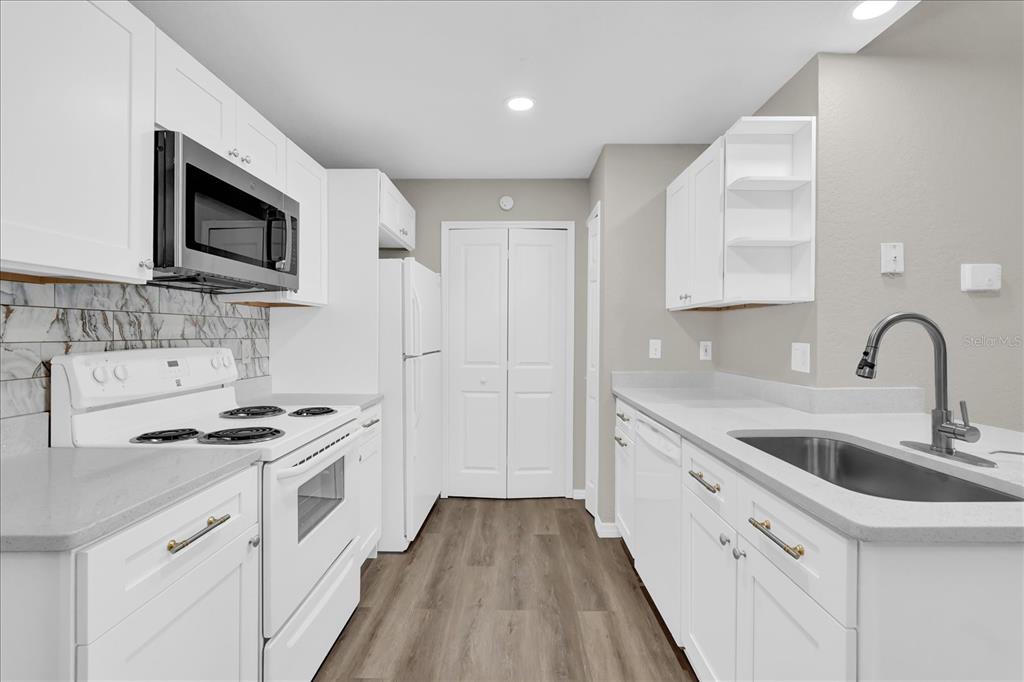 A kitchen features white cabinets, stainless steel appliances, a gray countertop, and wood-look flooring — 8915 LATREC AVENUE UNIT 2311, ORLANDO, FL