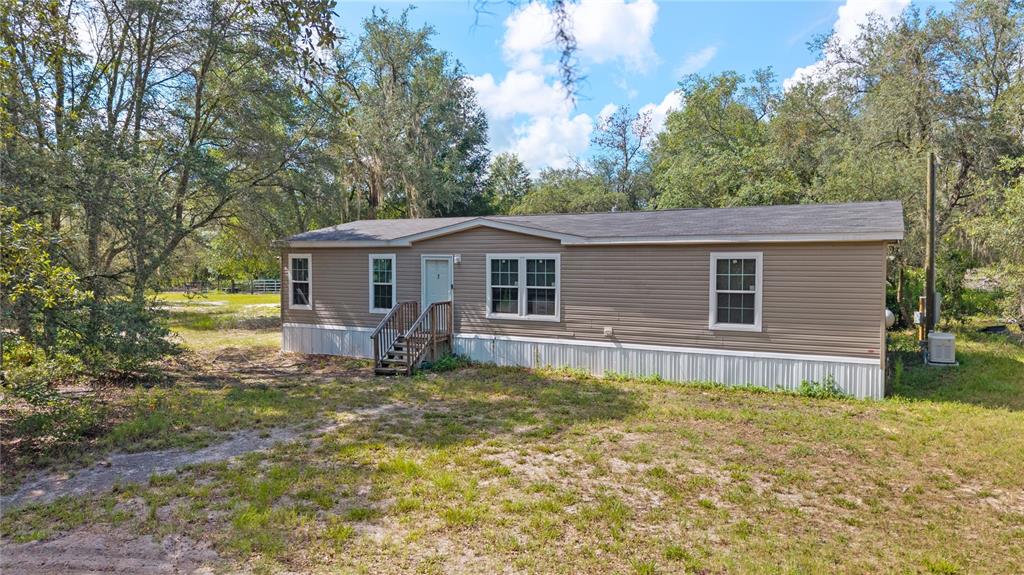 A single-story manufactured home with tan siding sits on a grassy lot among trees — 119 NE 98TH LANE, BRANFORD, FL