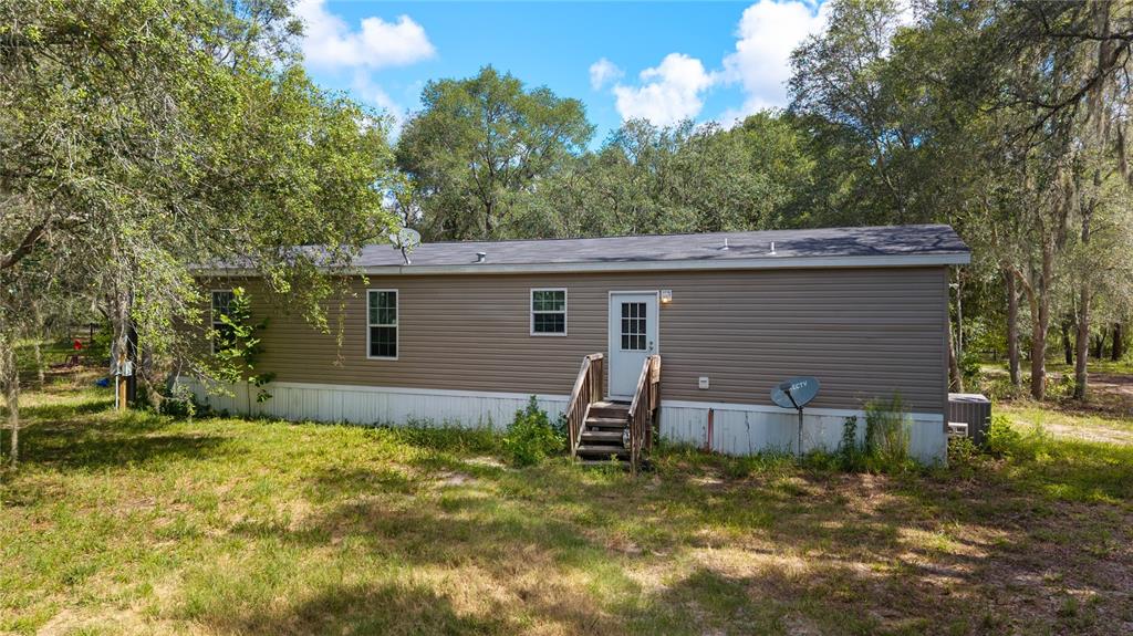 A tan mobile home with a white door and stairs sits in a wooded yard — 119 NE 98TH LANE, BRANFORD, FL