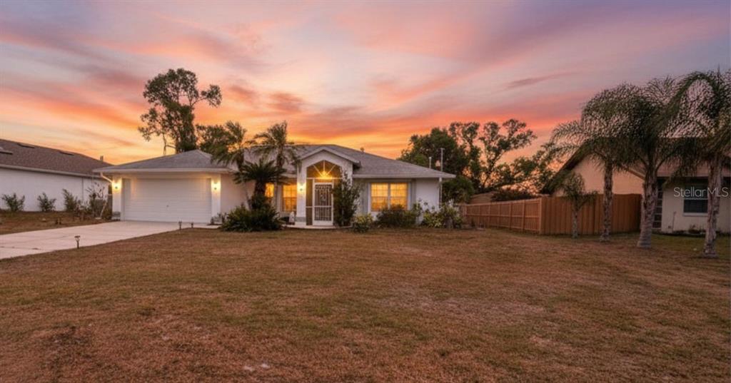 A single-story house with a white exterior, two-car garage, and palm trees at sunset — 22450 PEACHLAND BOULEVARD, PORT CHARLOTTE, FL