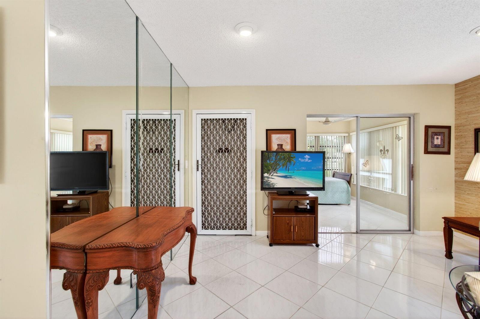 A room with white tile floors, mirrored walls, a television on a stand, and sliding doors — 14290 Nesting Way # A, Delray Beach FL 33484, DELRAY BEACH, FL