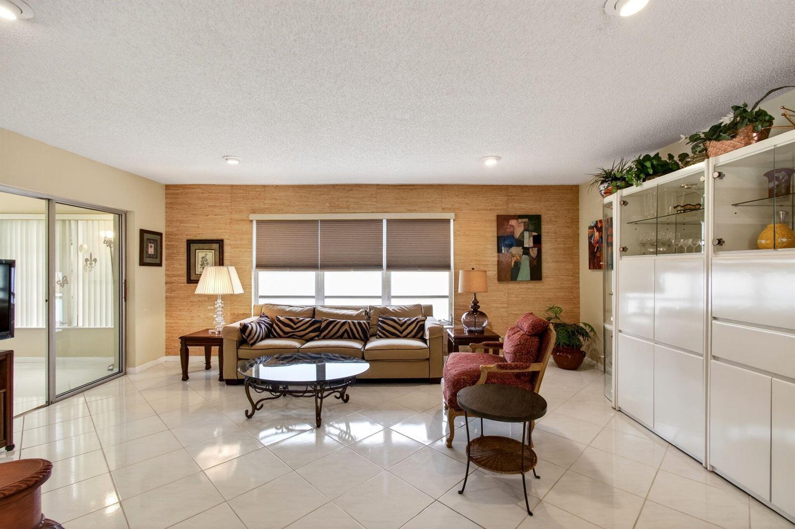 A living room features a beige sofa, a red armchair, and a textured wood-paneled wall — 14290 Nesting Way # A, Delray Beach FL 33484, DELRAY BEACH, FL
