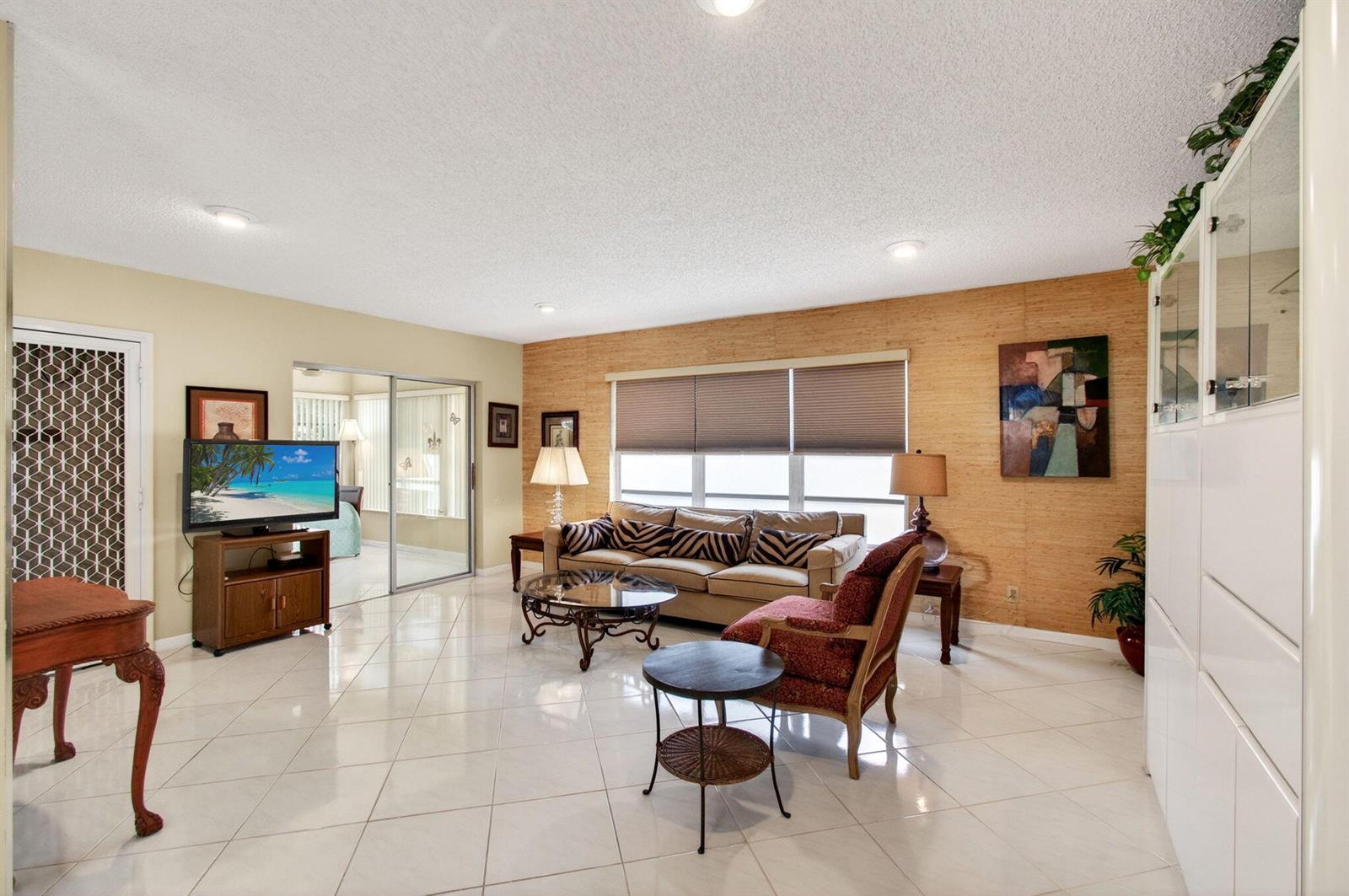 A living room features light tile floors, a textured accent wall, and a beige sofa — 14290 Nesting Way # A, Delray Beach FL 33484, DELRAY BEACH, FL