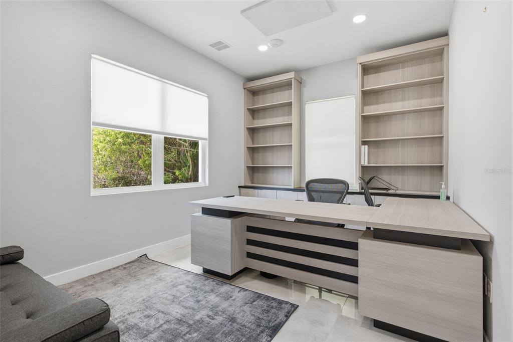 A home office features a light wood desk, matching built-in shelving, and a gray area rug — 13003 W LINEBAUGH AVENUE, TAMPA, FL