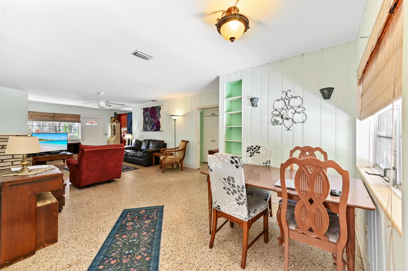 An open-concept living and dining area features light green paneled walls, terrazzo flooring, and furniture — 411 N Lakeside Drive, FL 33460, FL