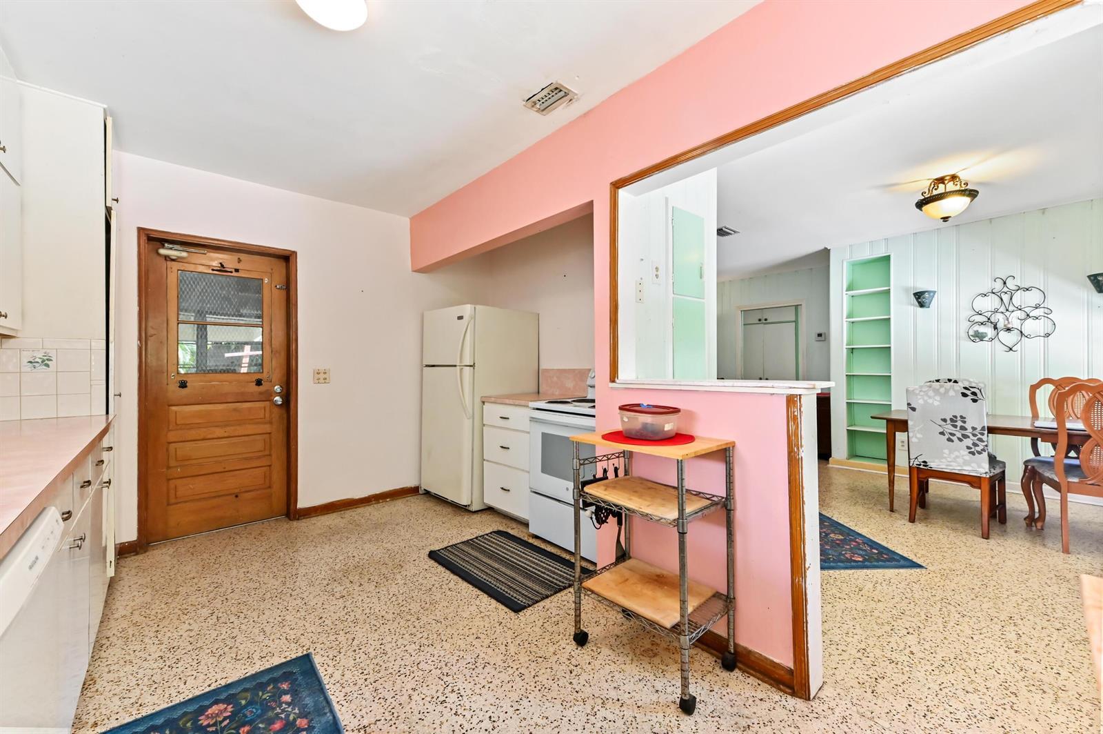 A kitchen with terrazzo floors, pink walls, and a wooden door opens to a dining area — 411 N Lakeside Drive, FL 33460, FL