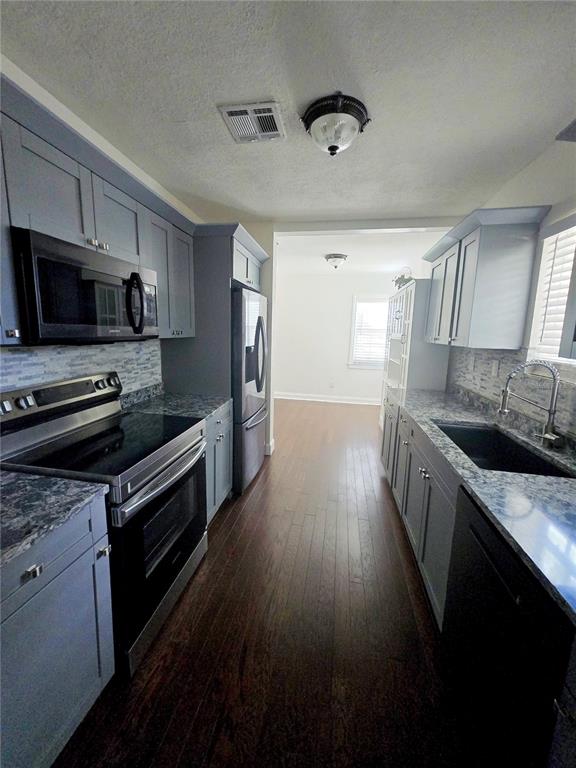 A galley kitchen features gray cabinets, dark countertops, stainless steel appliances, and wood flooring — 300 E IDLEWILD AVENUE, TAMPA, FL